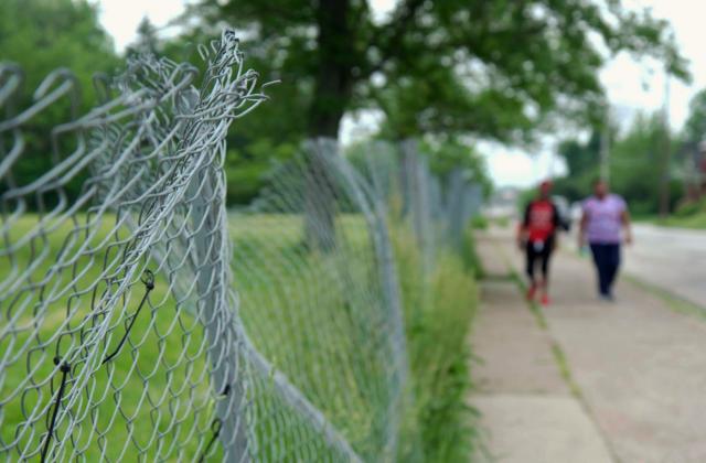 Broken fence and people walking down a sidewalk